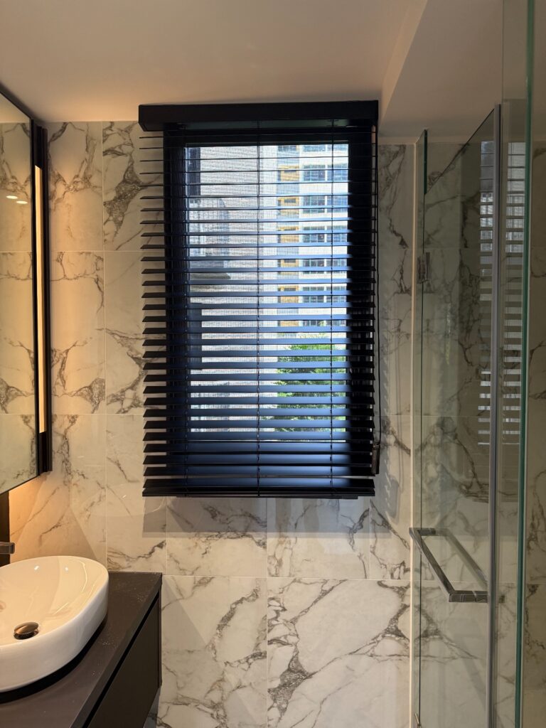 Black timber venetian blinds in a marble-tiled bathroom with a city view