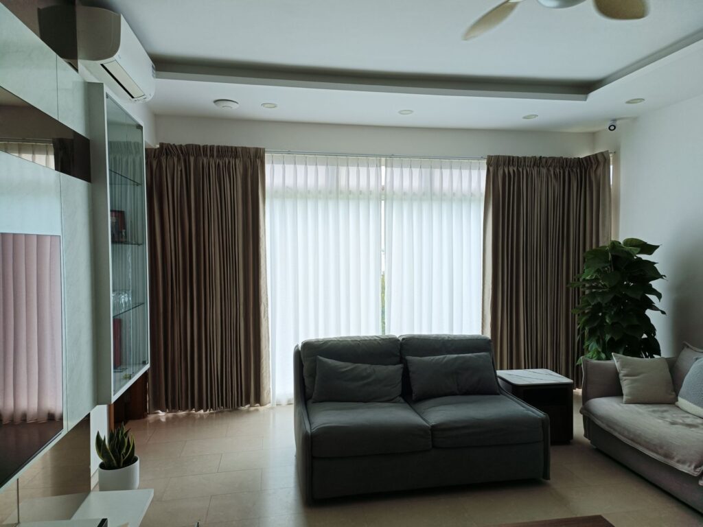 Floor-to-ceiling taupe pinch-pleat curtains with white sheers across full-height living room windows
